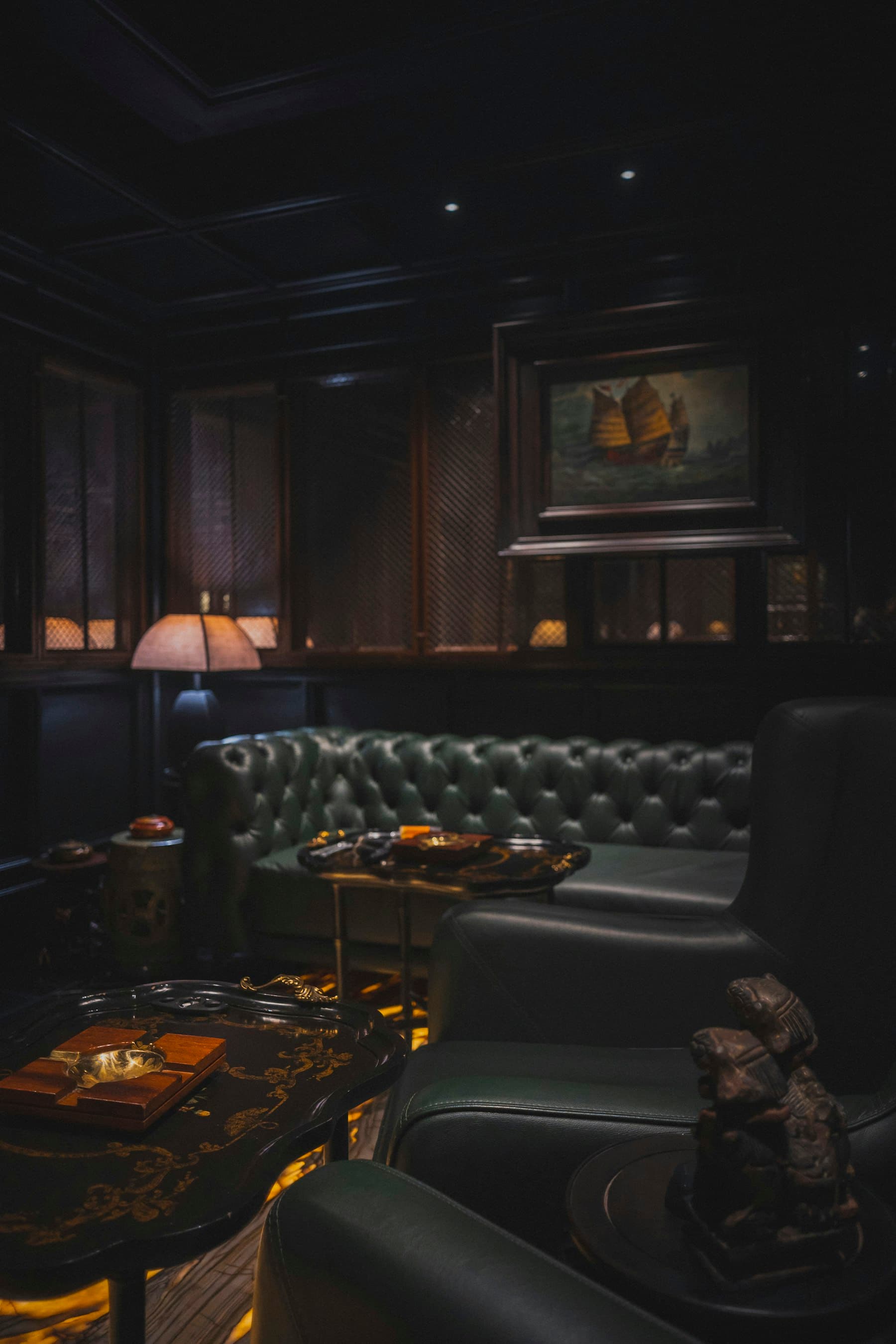 A dark cigar lounge with a tufted leather sofa and a warm lamp
